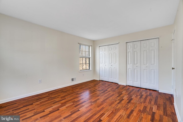 unfurnished bedroom with baseboards, visible vents, multiple closets, and wood finished floors