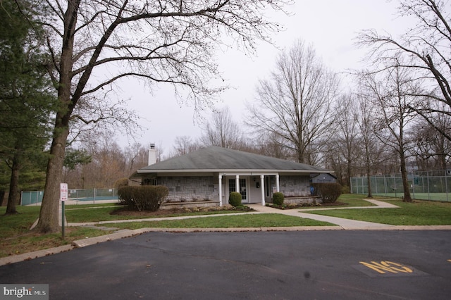 view of front of house with covered porch, fence, stone siding, a chimney, and a front yard