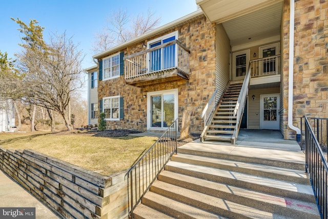 view of front of home featuring stone siding, stairway, and a front yard