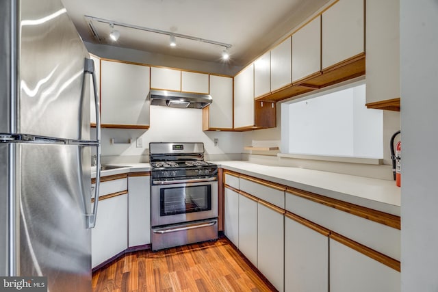 kitchen with appliances with stainless steel finishes, light countertops, under cabinet range hood, and wood finished floors