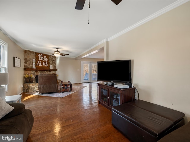 living room featuring wood finished floors, a ceiling fan, a fireplace, french doors, and crown molding