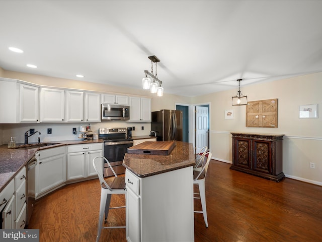 kitchen featuring dark wood-style floors, a breakfast bar, a sink, appliances with stainless steel finishes, and white cabinetry