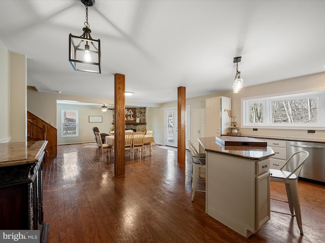 kitchen featuring a breakfast bar area, dark wood-style flooring, stainless steel dishwasher, decorative light fixtures, and a center island