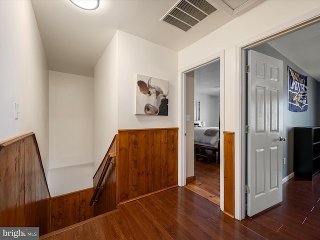 hall with an upstairs landing, visible vents, wainscoting, and dark wood-type flooring