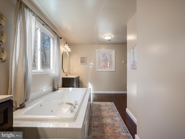 full bath with plenty of natural light, a whirlpool tub, wood finished floors, and vanity