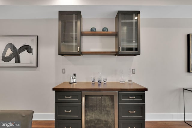 bar with dark wood-type flooring, beverage cooler, baseboards, and a bar