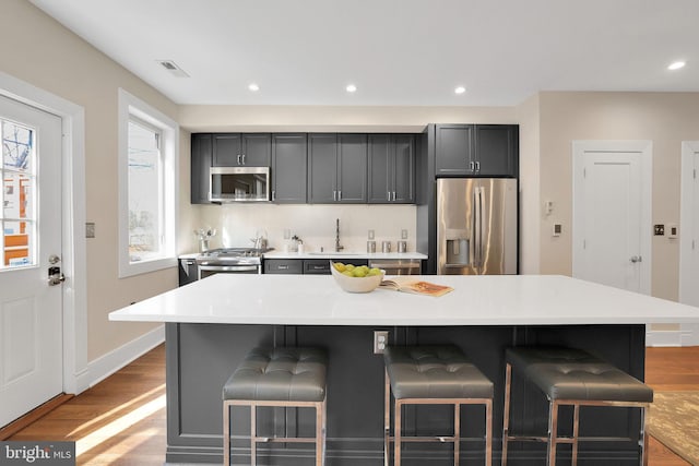 kitchen featuring visible vents, a breakfast bar, wood finished floors, stainless steel appliances, and a sink