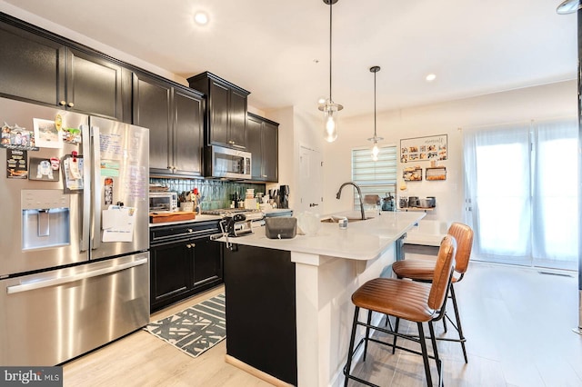 kitchen with stainless steel appliances, light countertops, backsplash, a sink, and a kitchen bar