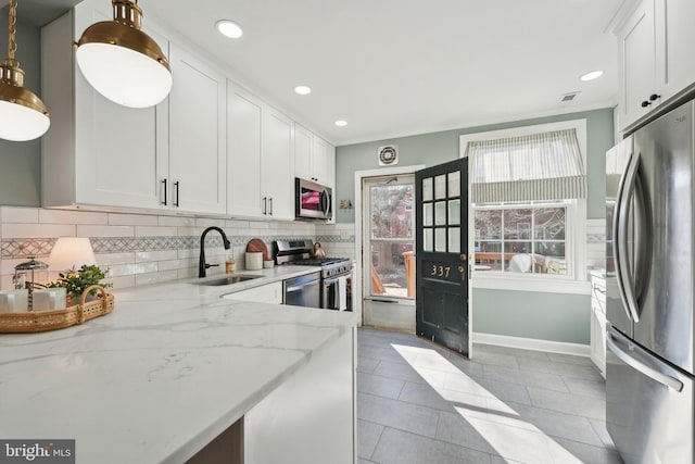 kitchen with light stone counters, a sink, stainless steel appliances, white cabinetry, and backsplash