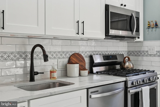 kitchen featuring a sink, light stone counters, tasteful backsplash, white cabinetry, and stainless steel appliances