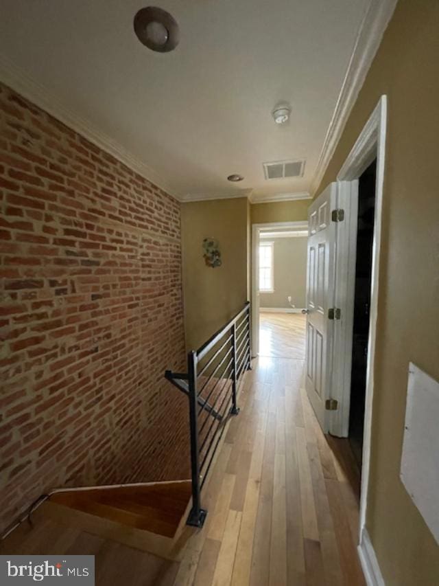 hallway with visible vents, light wood-style floors, ornamental molding, and brick wall