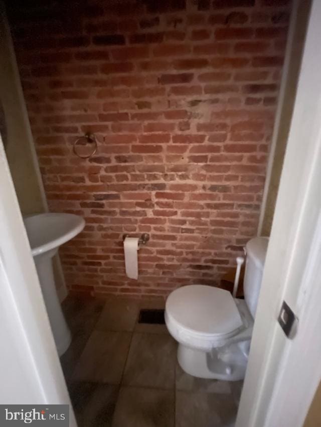 bathroom featuring tile patterned flooring, toilet, and brick wall