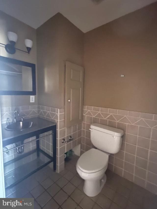 half bath with tile patterned floors, toilet, tile walls, and a wainscoted wall