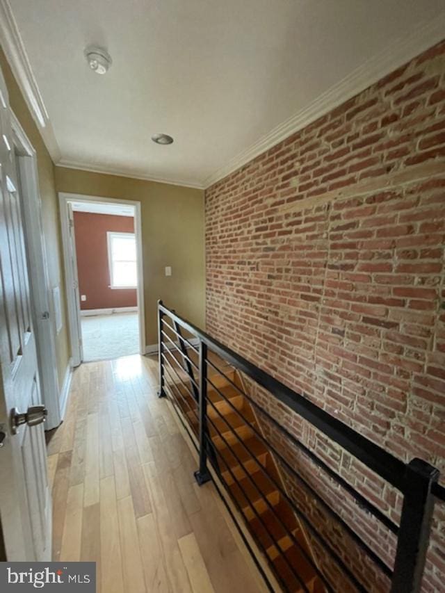 hallway with an upstairs landing, ornamental molding, light wood-style floors, brick wall, and baseboards