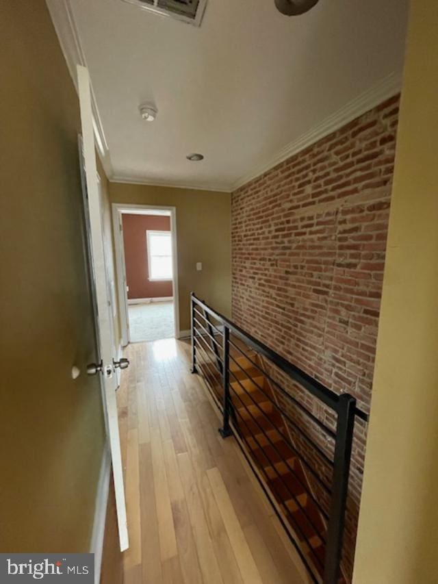 hall featuring light wood-type flooring, an upstairs landing, brick wall, crown molding, and baseboards