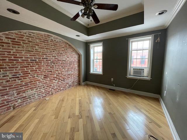 spare room with brick wall, baseboards, ornamental molding, wood finished floors, and a raised ceiling