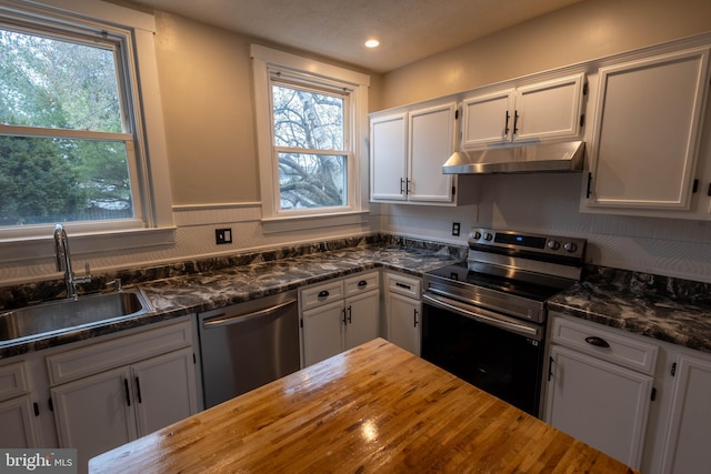 kitchen featuring white cabinets, butcher block counters, stainless steel appliances, under cabinet range hood, and a sink