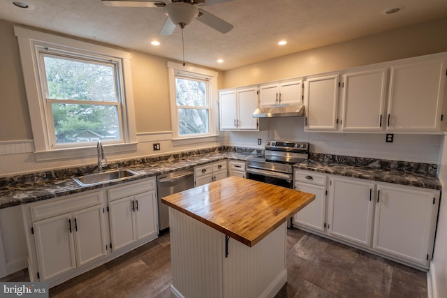 kitchen featuring butcher block counters, appliances with stainless steel finishes, white cabinets, a sink, and under cabinet range hood