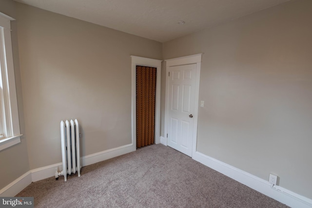 empty room with carpet floors, radiator heating unit, and baseboards