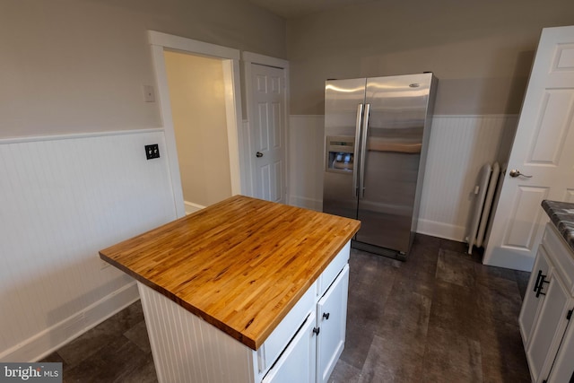 kitchen with a center island, a wainscoted wall, white cabinets, wood counters, and stainless steel fridge with ice dispenser