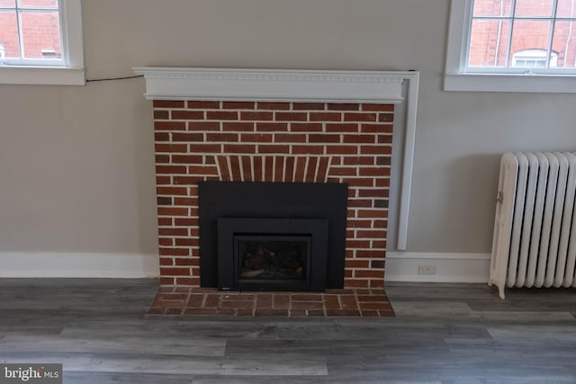 interior details with radiator heating unit, a brick fireplace, wood finished floors, and baseboards