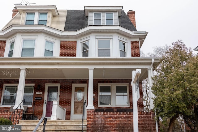 townhome / multi-family property featuring brick siding, a porch, and a shingled roof