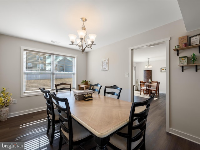 dining space featuring dark wood-style flooring, visible vents, and an inviting chandelier