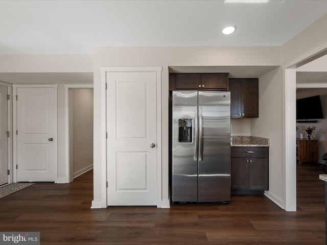 kitchen with light stone counters, dark wood-style flooring, dark brown cabinets, and stainless steel fridge with ice dispenser