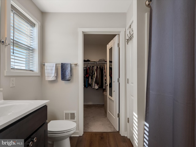 bathroom with curtained shower, toilet, wood finished floors, vanity, and visible vents