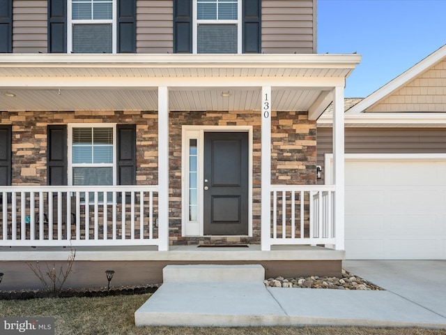 entrance to property featuring a garage, stone siding, and covered porch