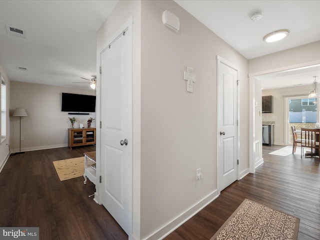 hallway with visible vents, baseboards, and dark wood-type flooring