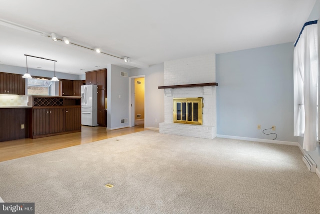 unfurnished living room with a fireplace, rail lighting, light colored carpet, visible vents, and baseboards