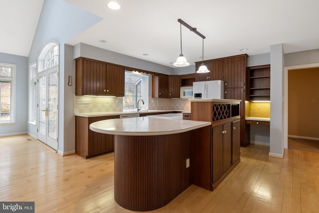 kitchen featuring white appliances, light countertops, light wood-type flooring, backsplash, and a center island