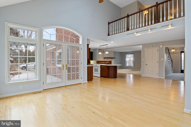 unfurnished living room featuring baseboards, a towering ceiling, stairway, french doors, and light wood-style floors