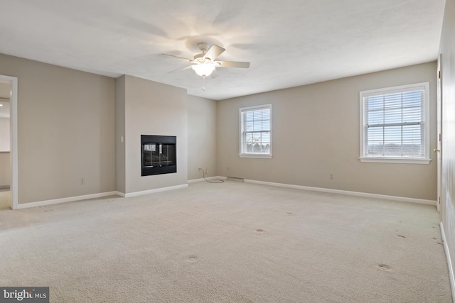 unfurnished living room featuring a glass covered fireplace, light carpet, ceiling fan, and baseboards