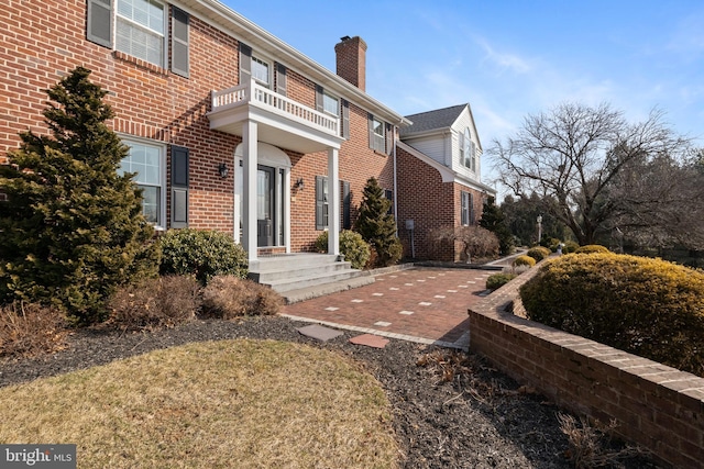 view of property exterior with a chimney, brick siding, and a balcony