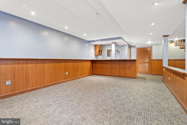 interior space with brown cabinets, a wainscoted wall, wood walls, and carpet flooring