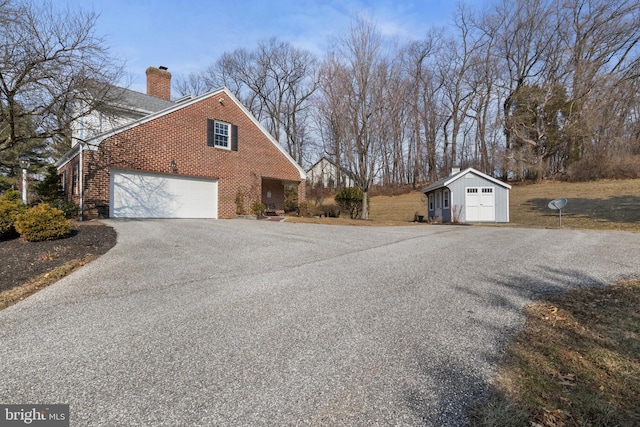 view of side of property with driveway, a garage, a chimney, an outbuilding, and brick siding