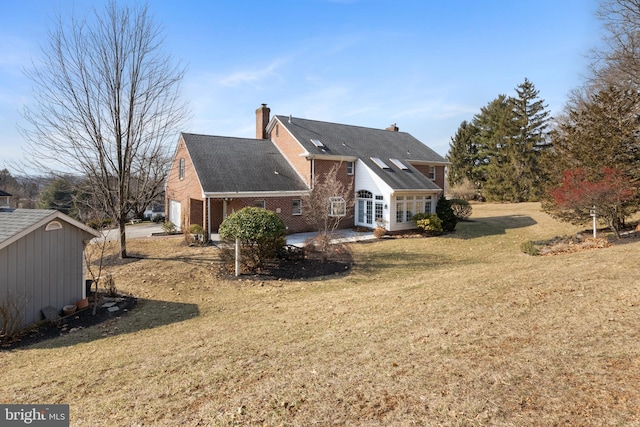 back of property featuring a garage, brick siding, a lawn, a chimney, and a patio area