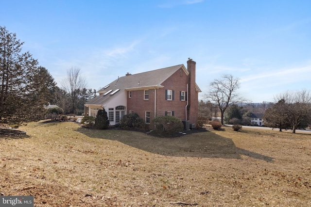 view of side of property with brick siding, a lawn, and a chimney