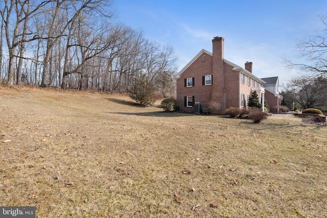 view of side of property featuring brick siding, a yard, a chimney, and central AC unit