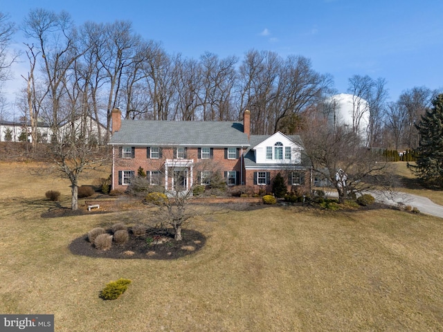 colonial inspired home featuring brick siding, a chimney, and a front yard