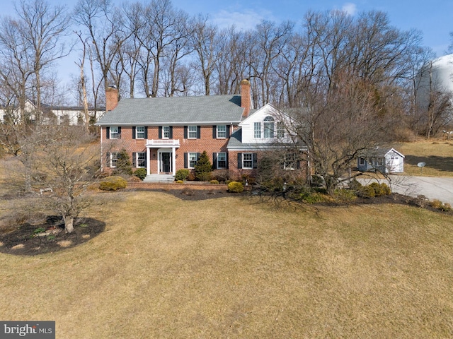 view of front of house with brick siding, a chimney, and a front lawn