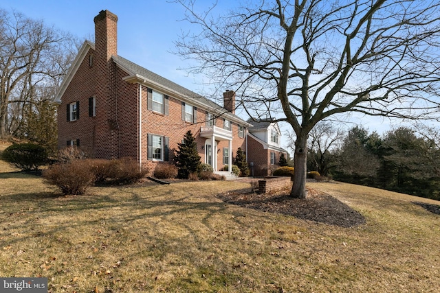 view of side of property with brick siding, a lawn, and a chimney