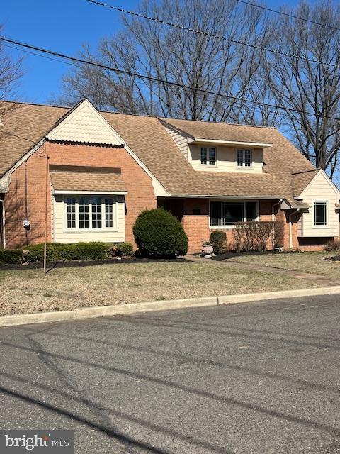 view of front of property featuring brick siding, a front lawn, and roof with shingles