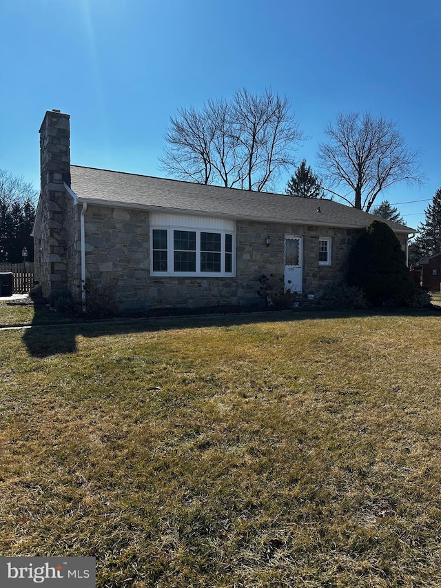 view of front of house featuring stone siding, roof with shingles, a chimney, and a front lawn