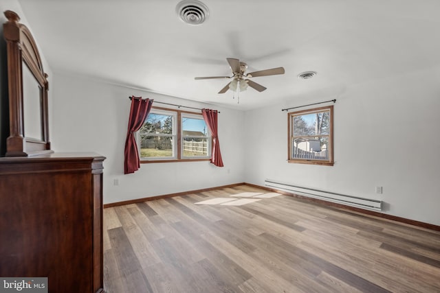 unfurnished bedroom featuring a baseboard heating unit, baseboards, visible vents, and wood finished floors