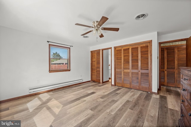 unfurnished bedroom with visible vents, multiple closets, wood finished floors, a baseboard radiator, and baseboards