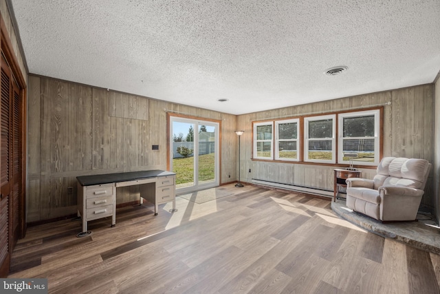 unfurnished living room featuring a baseboard heating unit, a textured ceiling, visible vents, and wood finished floors