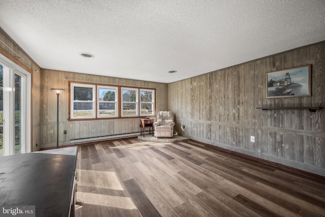 unfurnished room featuring visible vents, wooden walls, wood finished floors, a textured ceiling, and a baseboard radiator